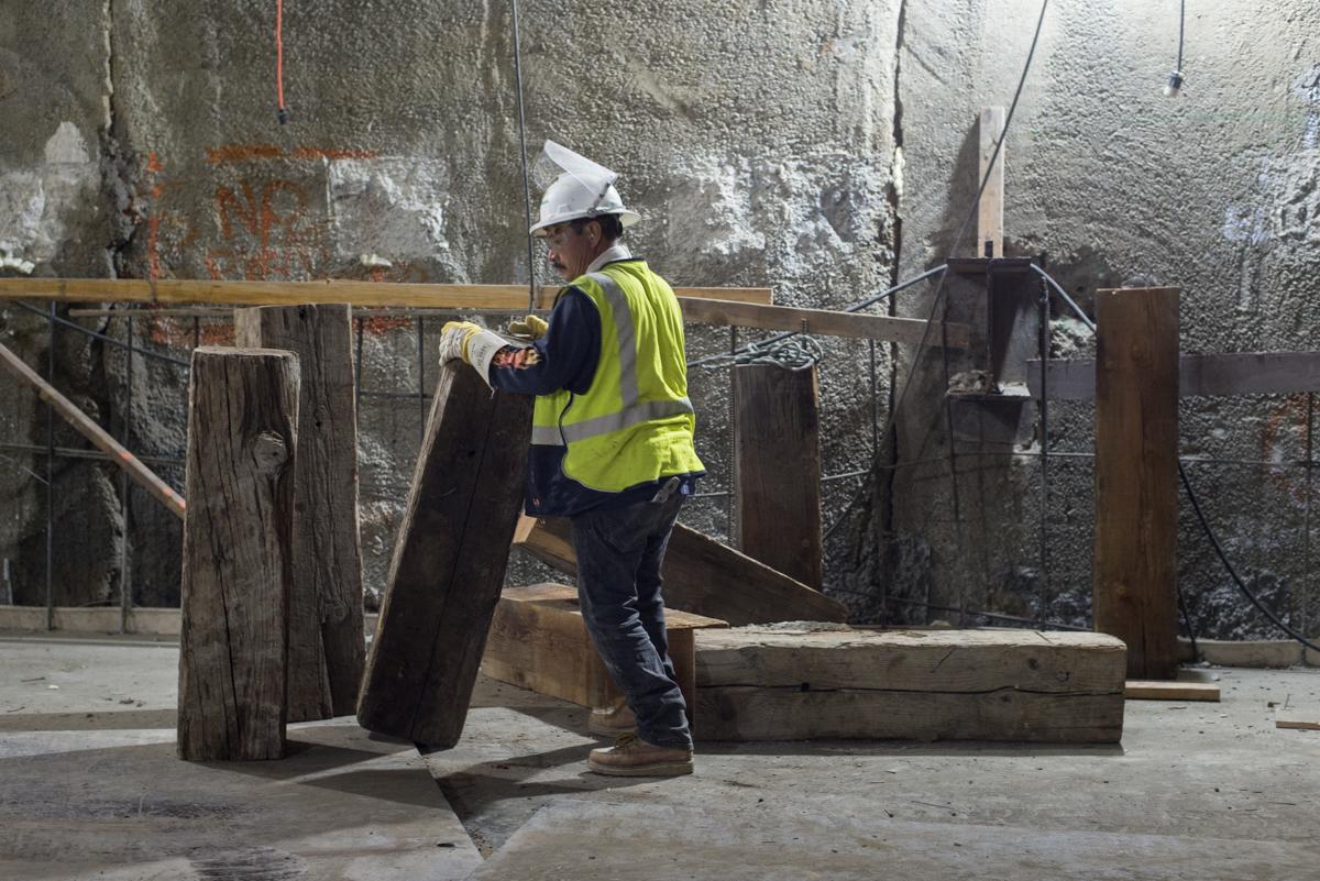 Worker in safety vest and hard hat positioning wooden support beam at underground transit station construction site.