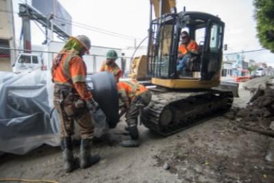 Workers in orange vests operate excavator during sewer line installation on 4th Street.