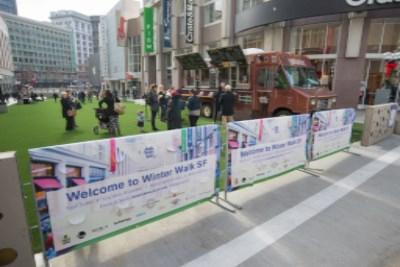 Winter Walk 2015 street fair with banners, food truck, and visitors in downtown plaza.