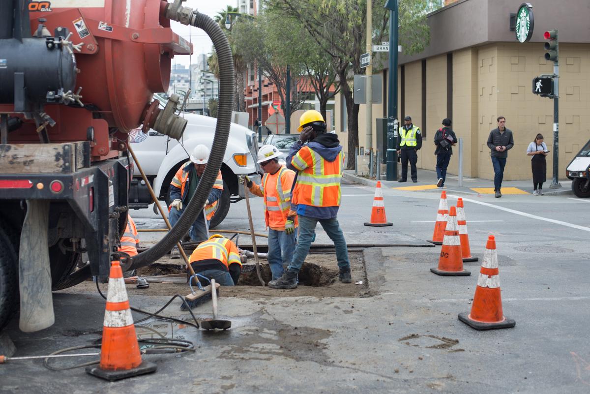 Workers operate a vacuum truck to remove material from a street trench during utility upgrade work.