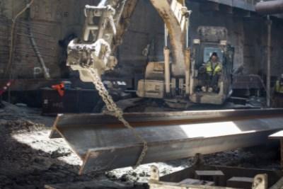 Excavator lifting steel I-beam at underground transit station construction site