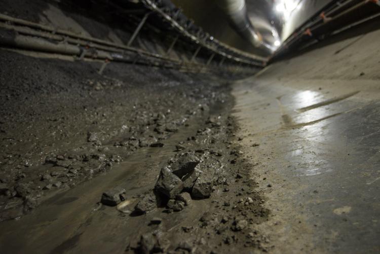 Tunnel boring machine excavation showing fragmented bedrock debris on tunnel floor under bright work lights.