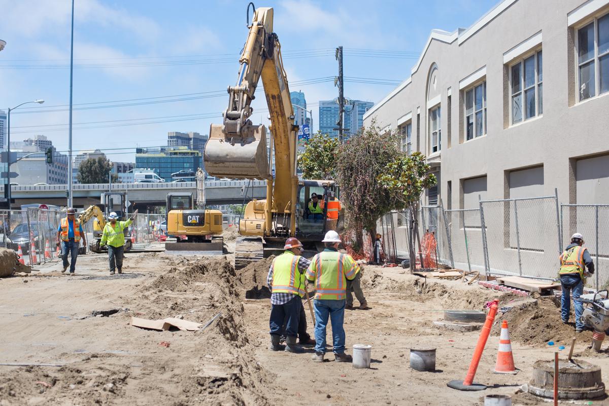 Construction crew excavating underground utility line with CAT excavator on urban street.