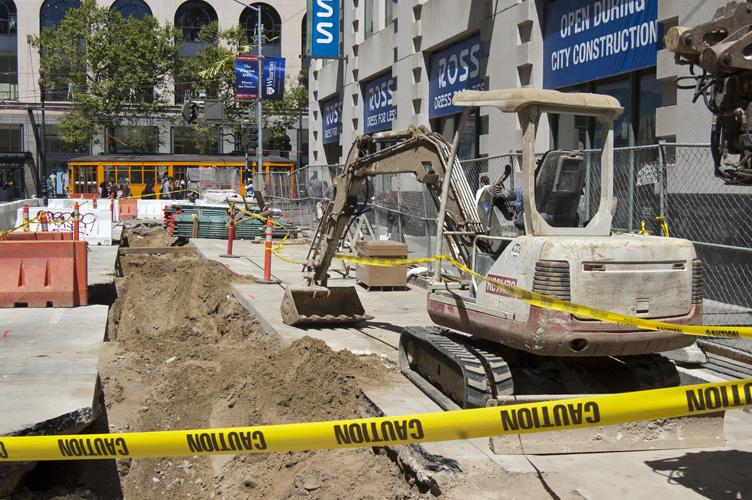 Construction excavator operating on 4th Street with yellow caution tape, red barriers, and construction signage visible.