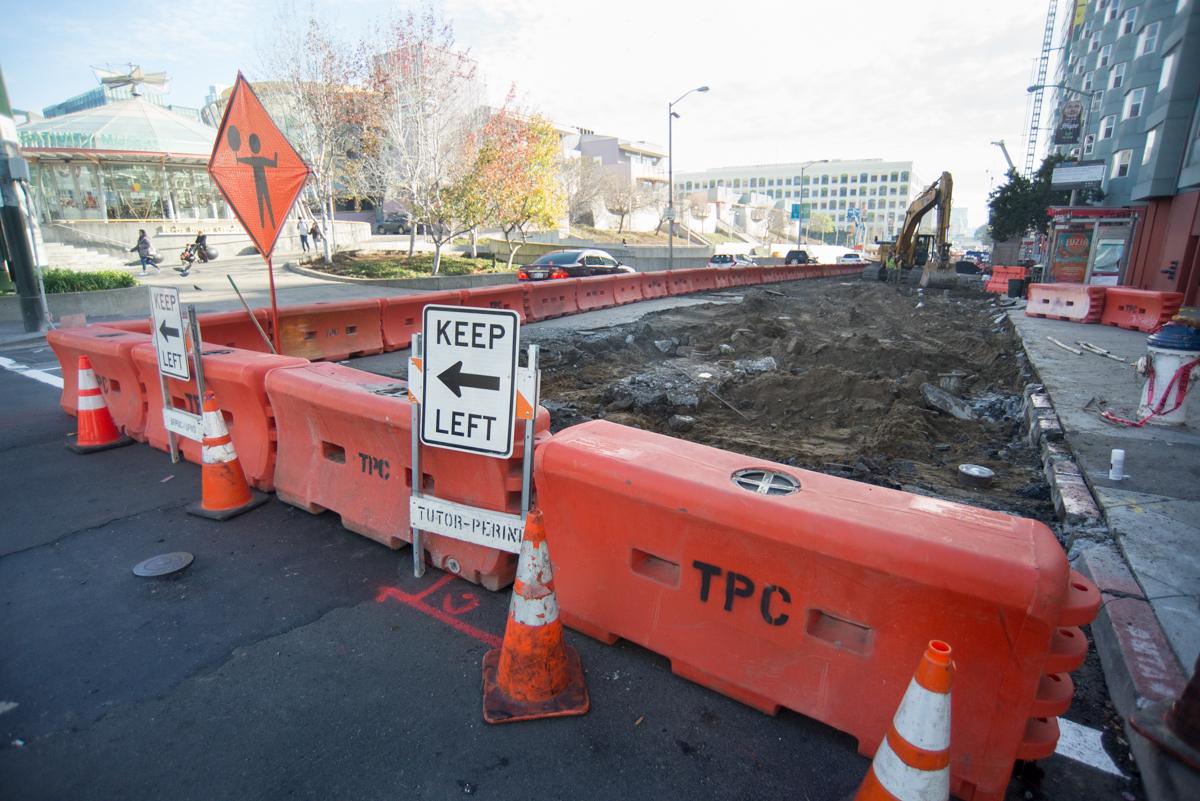 Construction site with red barriers, warning signs, and excavation equipment on urban street.