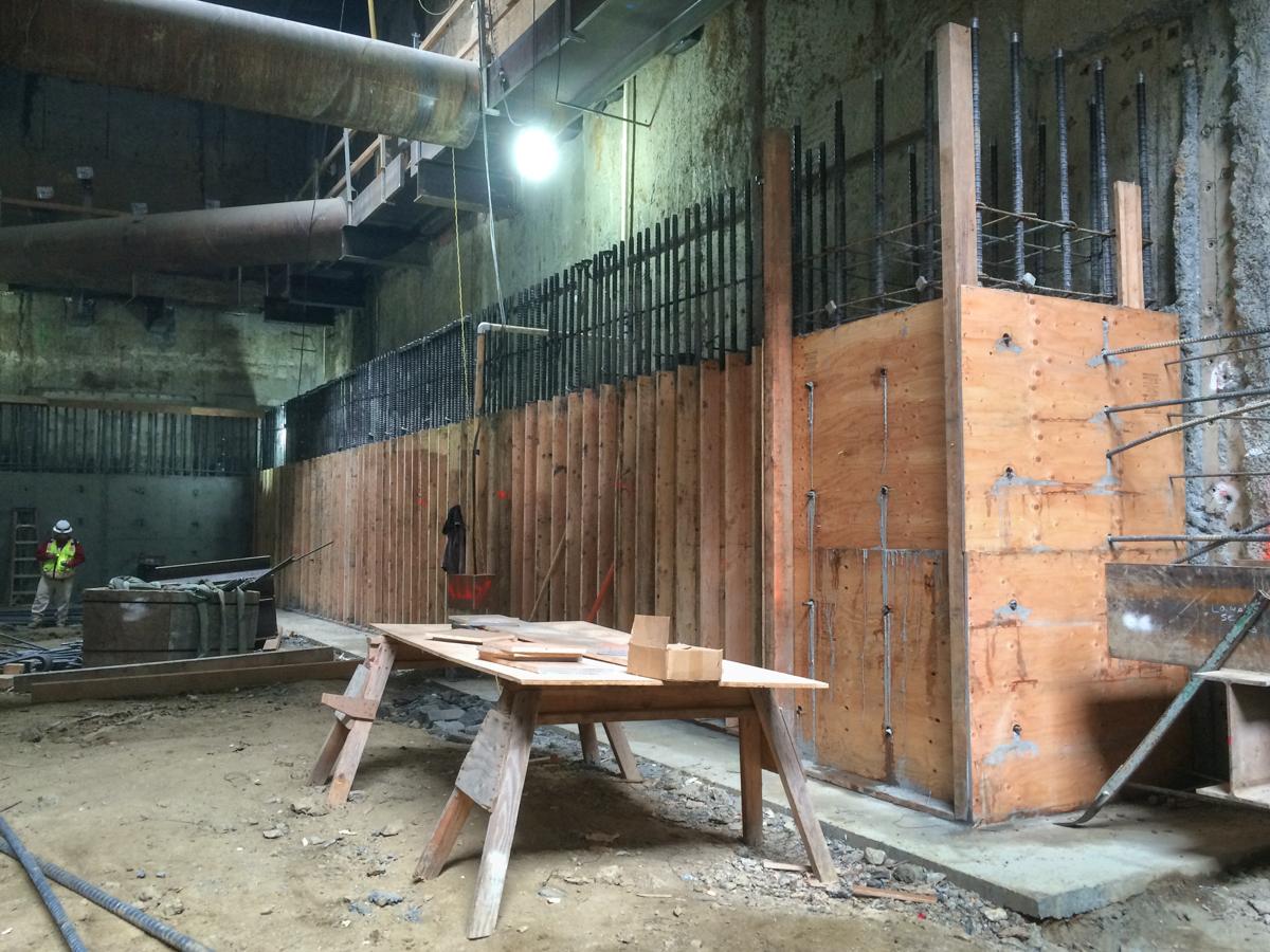 Construction site with wooden structural framing, metal scaffolding, and work materials inside an underground station headhouse.