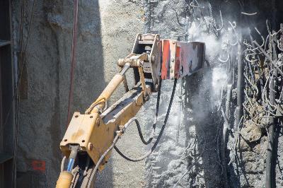 Jackhammer operator sprays water while breaking up concrete at a slurry wall construction site.
