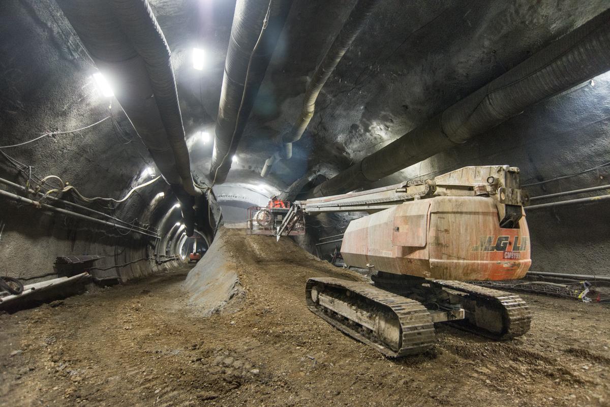 Excavator with jackhammer breaking apart tunnel lining segments inside underground station cavern.