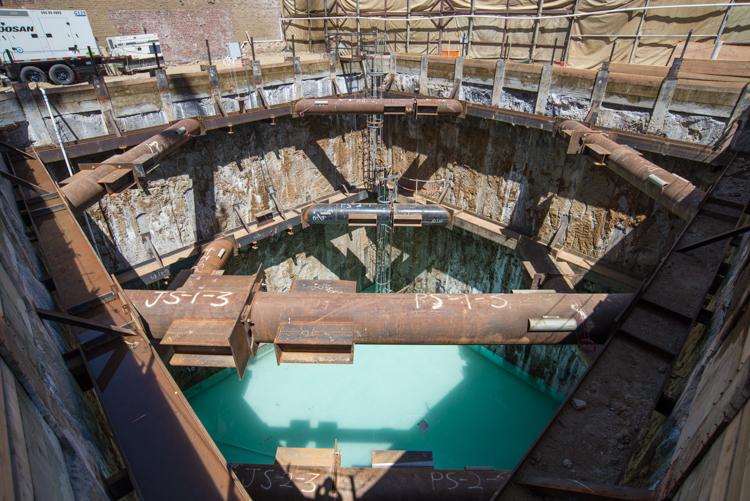 TBM retrieval shaft with turquoise groundwater, steel support structures, and construction equipment visible above.