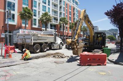Construction crew operating excavator and dump truck on King Street for sewer line installation.