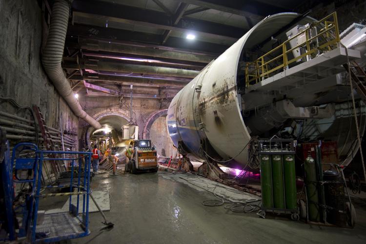 Large tunnel boring machine under assembly in underground construction tunnel with equipment and workers.