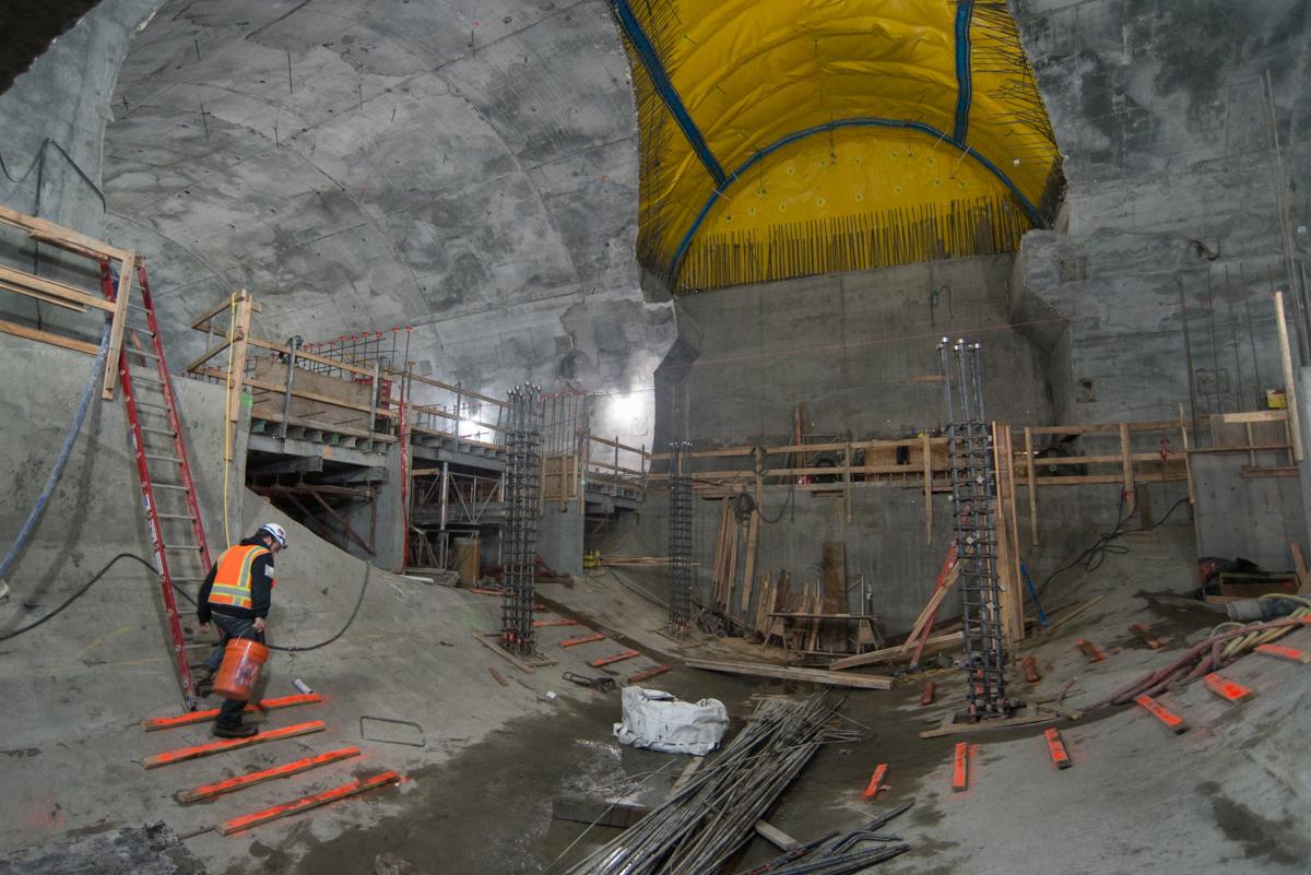 Worker in safety gear inside underground tunnel with yellow ventilation duct and construction materials.