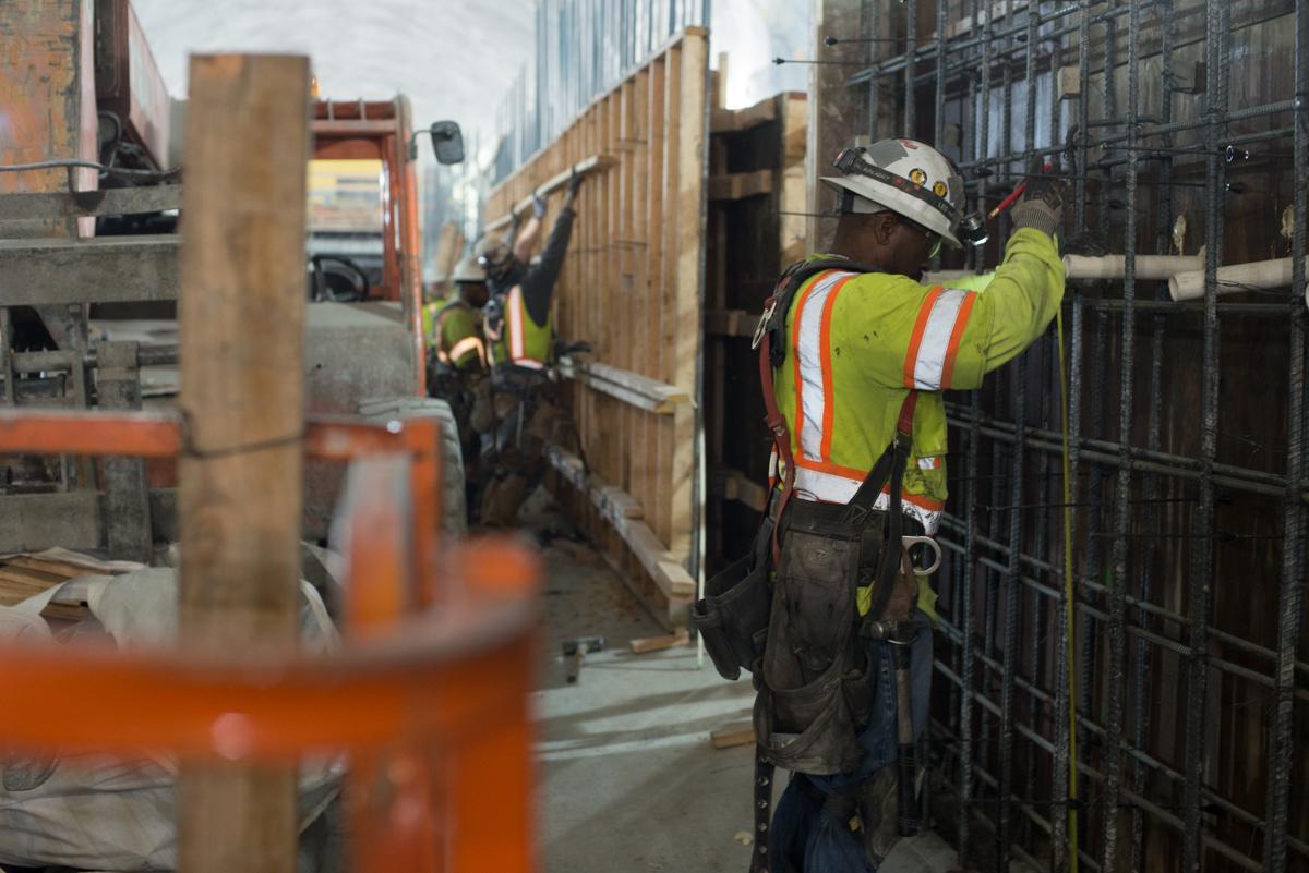 Construction worker in safety gear installing rebar reinforcement in underground transit station cavern.