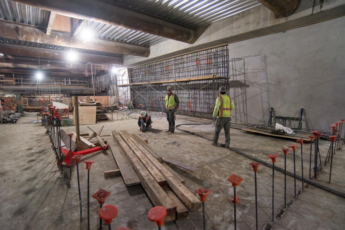Construction workers install temporary railings around wooden beams in an underground transit station.