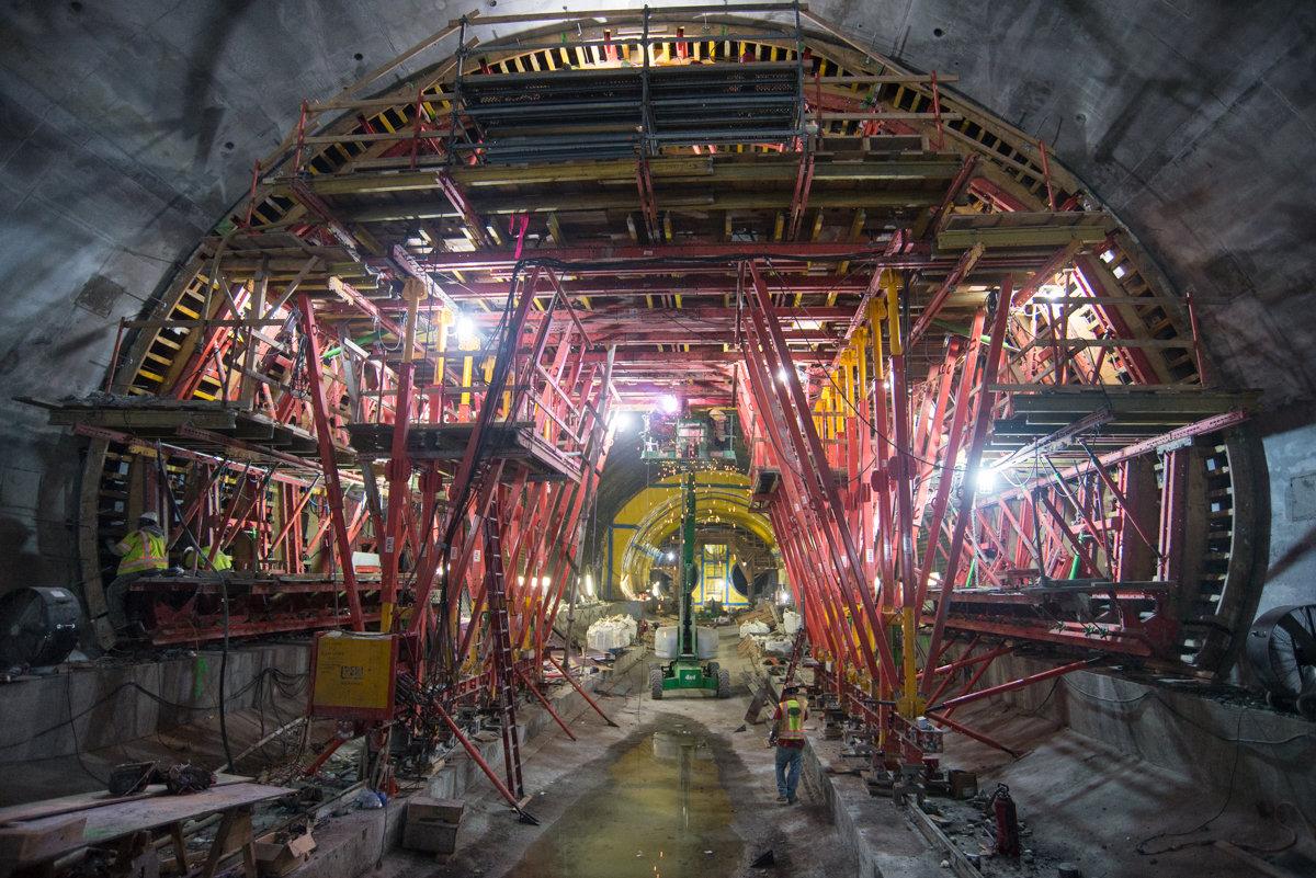 Underground tunnel construction showing red steel truss formwork and support structures along Stockton Street.