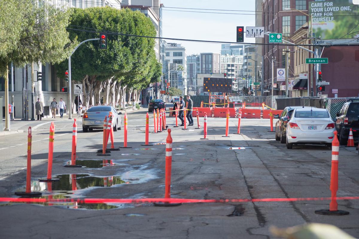 Street intersection closed with red and white barriers and orange cones marking construction work zones.