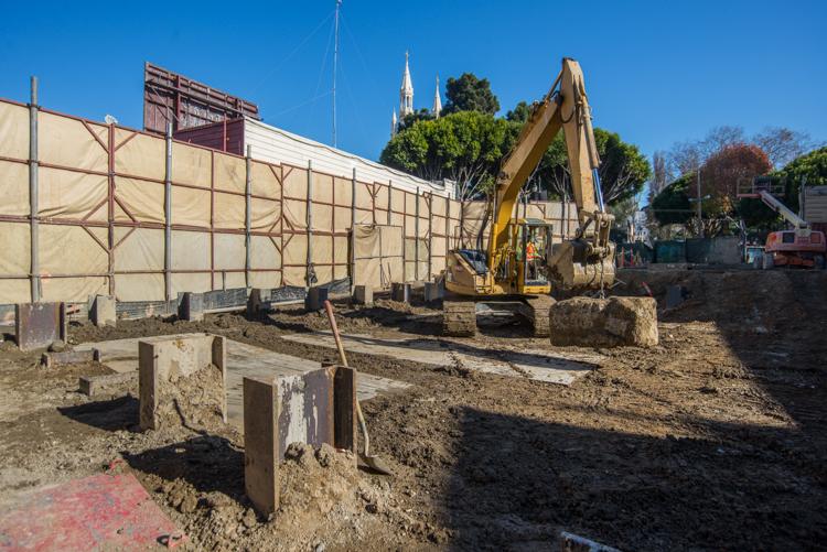 Construction site with excavator, wooden posts, and protective fencing near Powell Street
