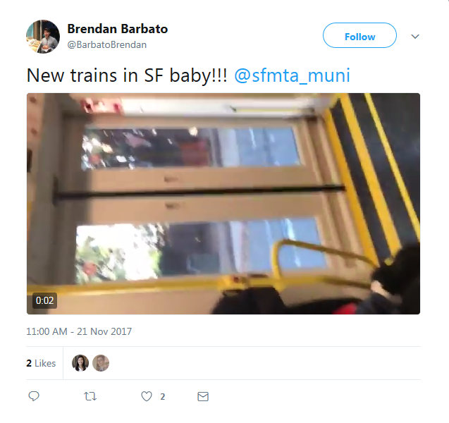 Interior view of new SFMTA train car with yellow and black striped handrail and windows showing city street.