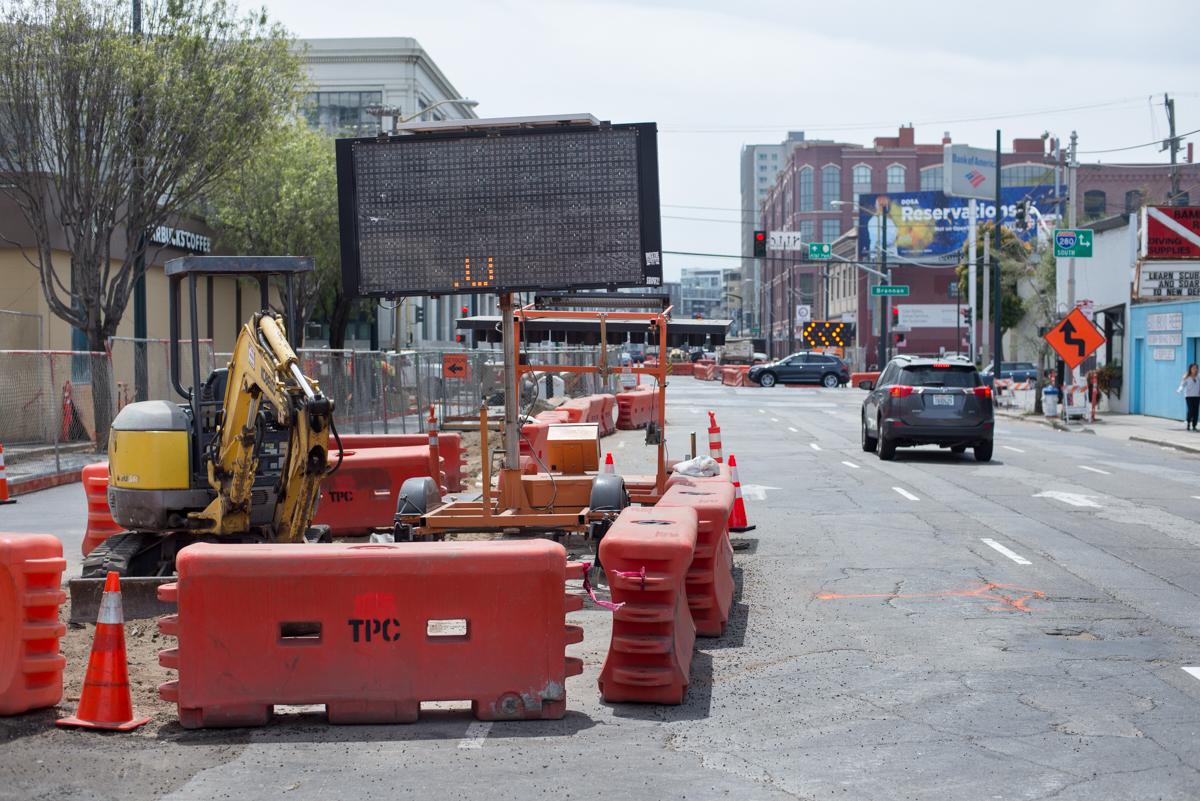 Construction equipment and red barriers block 4th Street during utility work, with digital sign and city buildings visible.