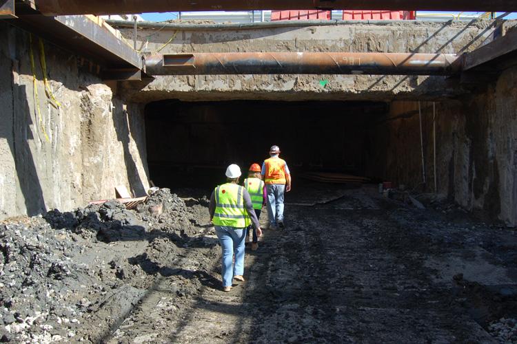 Construction workers in safety gear inside underground tunnel launch box at Central Subway project site.