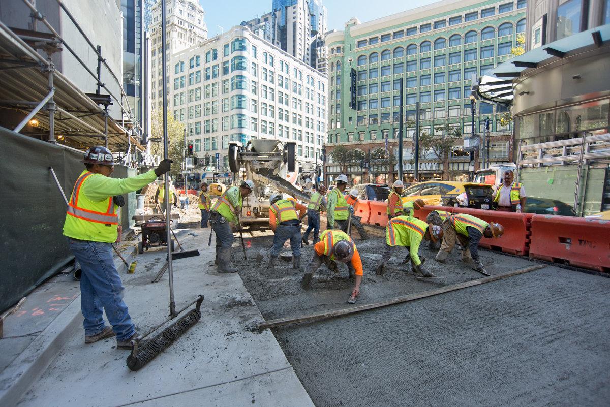 Construction crew in high-visibility vests working on street repaving and concrete restoration on Ellis Street in downtown San Francisco.