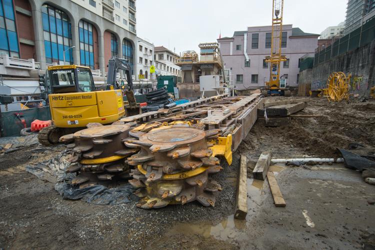 Construction site with yellow excavator, hydromill equipment, and building materials at Chinatown Station property.