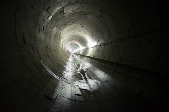 Worker in concrete tunnel with overhead lighting, Central Subway construction.
