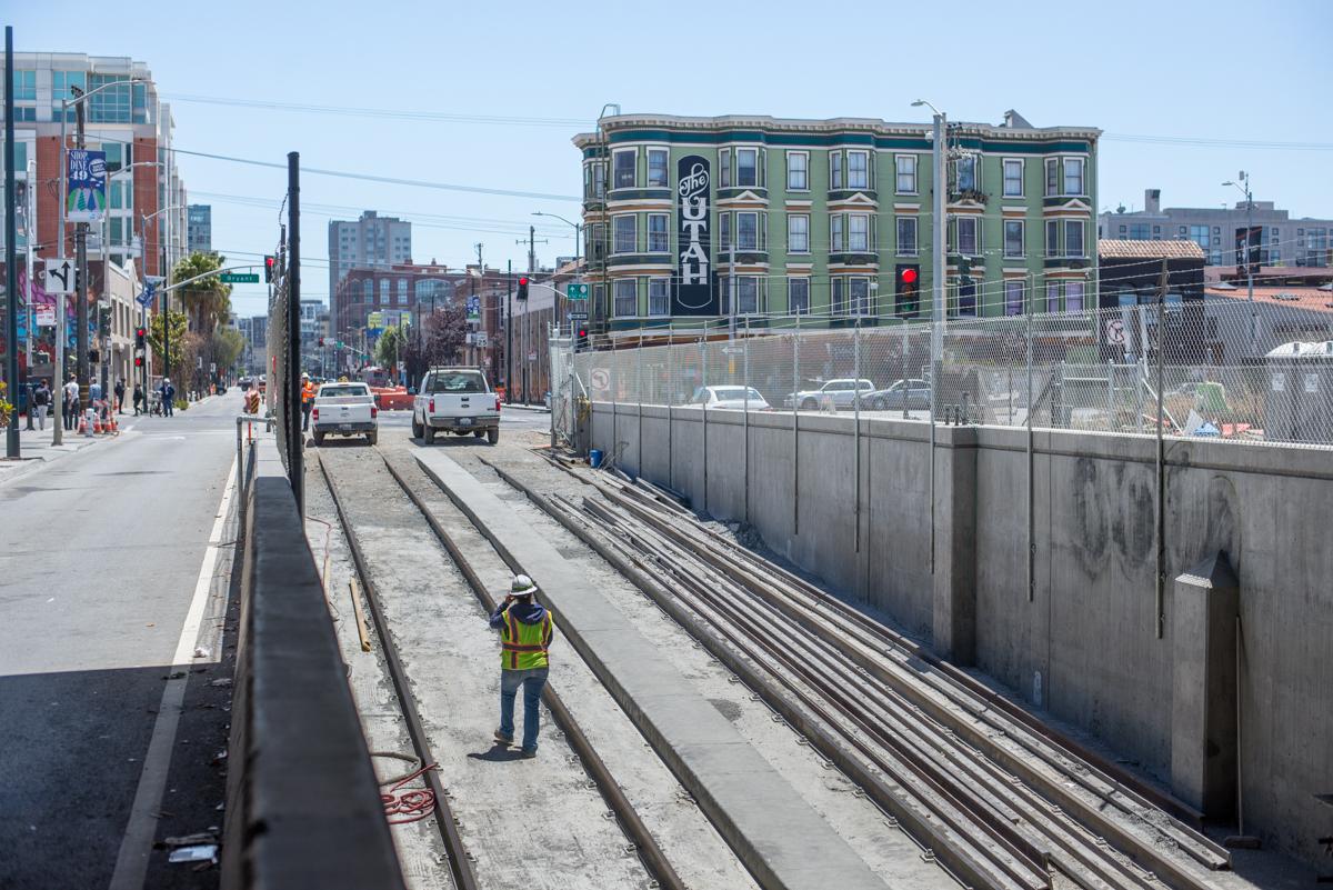 Worker in safety vest stands on light rail tracks during platform construction at Yerba Buena/Moscone Station.