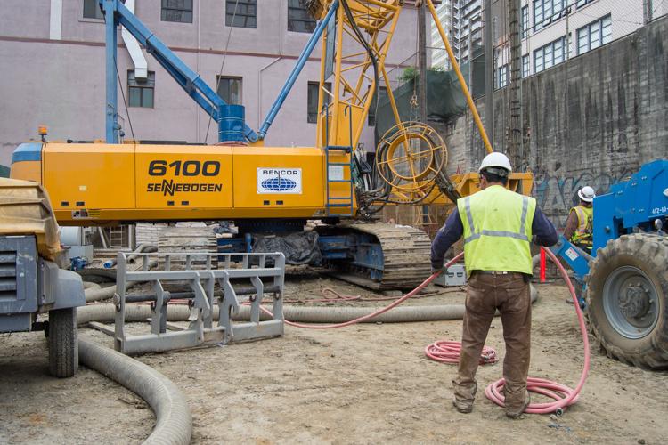 Construction workers operate concrete pump and excavation equipment at Chinatown Station site.