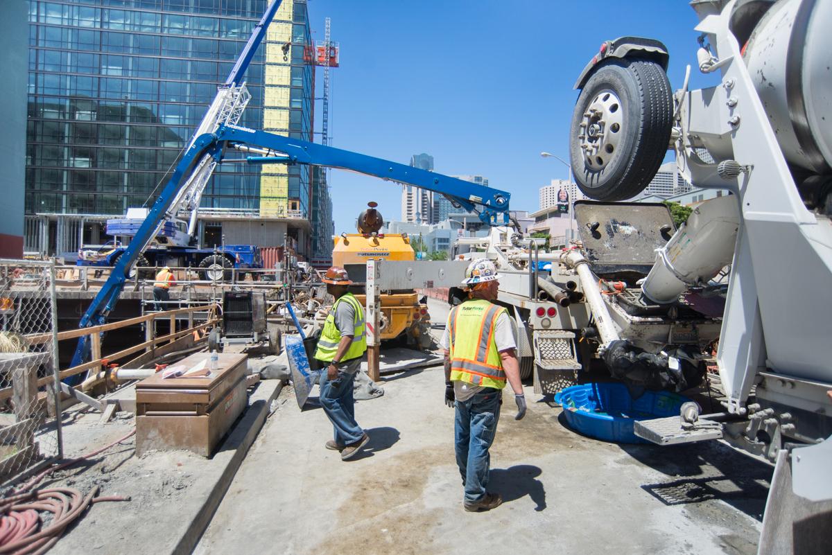 Construction workers in safety vests near concrete pump truck and construction equipment at urban job site.