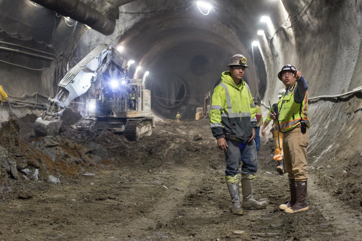 Two workers in safety vests inspect tunnel construction inside Chinatown station headhouse.