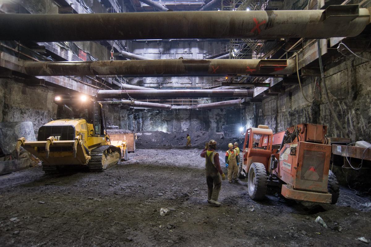 Workers and heavy equipment excavate underground platform cavern at transit station construction site.
