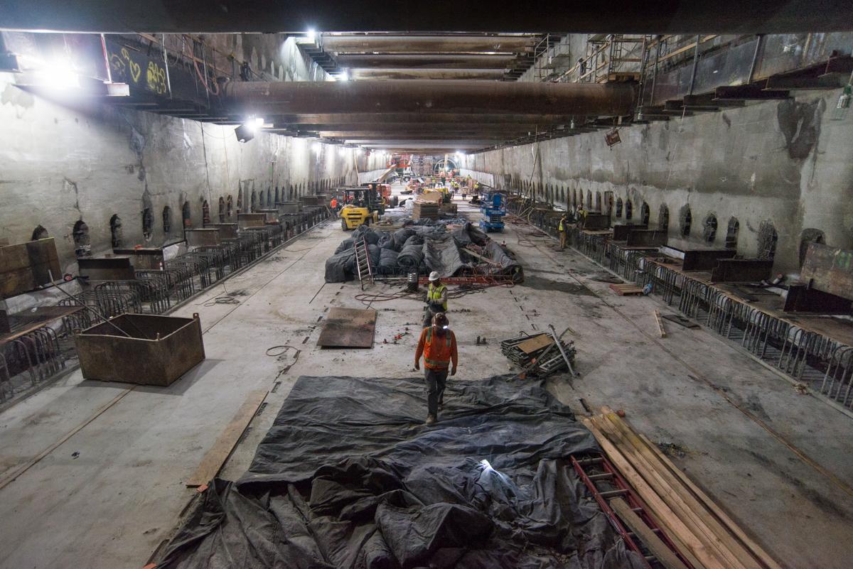 Workers remove temporary steel bracing from underground transit station construction site.