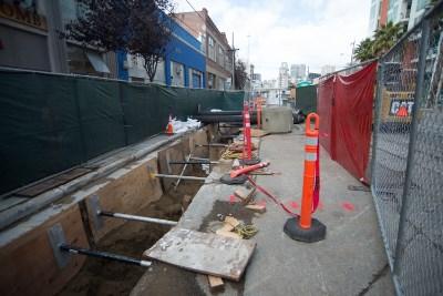Construction trench with utility work, orange safety barriers, and equipment on city street.