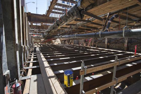 Construction site showing wooden framing and steel beams for roof deck installation between floor joists.