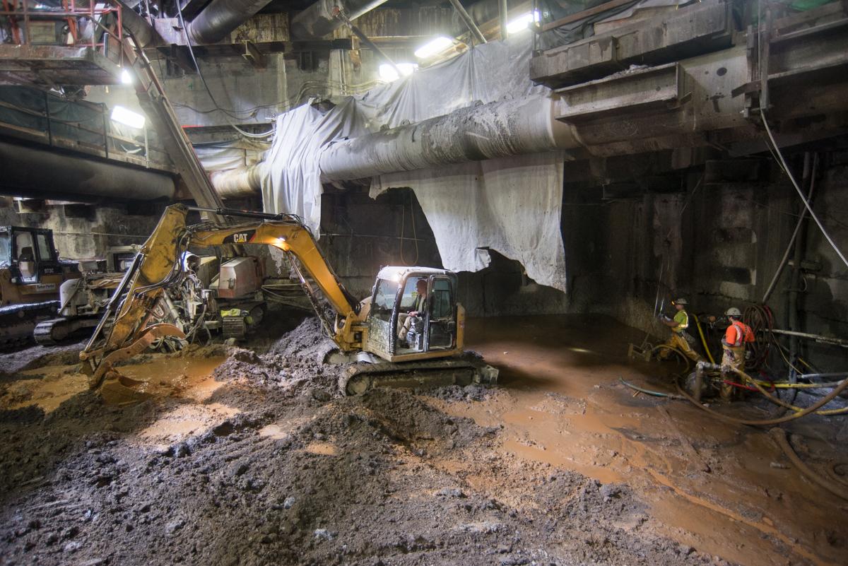 Excavation equipment and workers inside underground station cavern during soil improvement drilling operations.