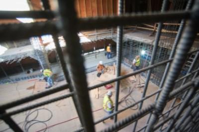 Construction workers in safety vests work on pile installation at Geary and Stockton intersection behind protective fencing.