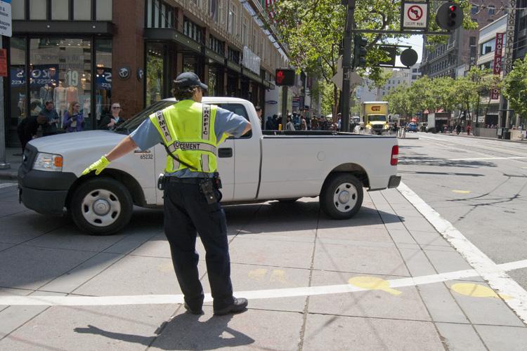 Traffic control officer in yellow safety vest directing vehicle on city street at 4th and Market.