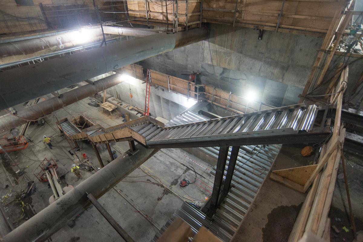 Construction of new staircase and platform infrastructure in underground transit station with workers and equipment.