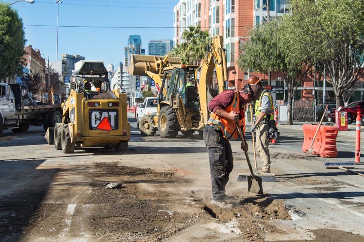 Workers excavate utilities on 4th Street with heavy equipment and orange safety barriers visible.