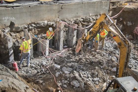 Workers in safety gear operate excavator removing concrete debris at underground construction site.