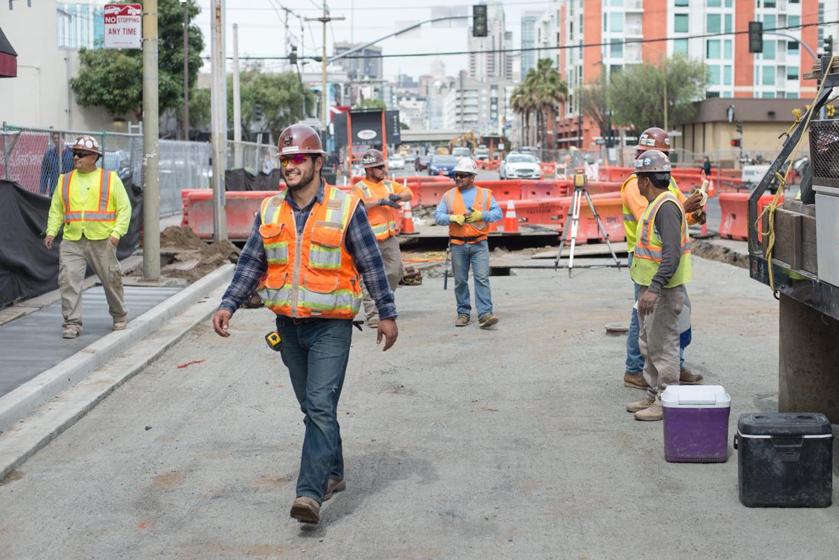 Construction workers in safety vests and hard hats on 4th Street work site with equipment and barriers visible.