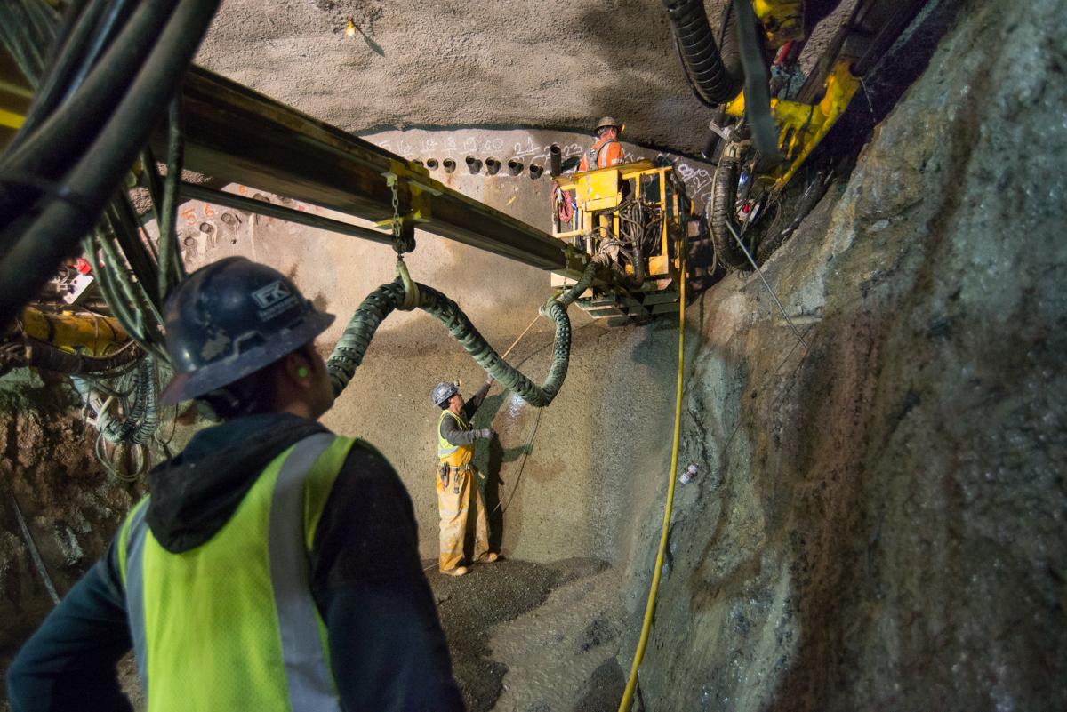 Workers in safety gear and harnesses operate equipment inside an underground cavern during maintenance work.