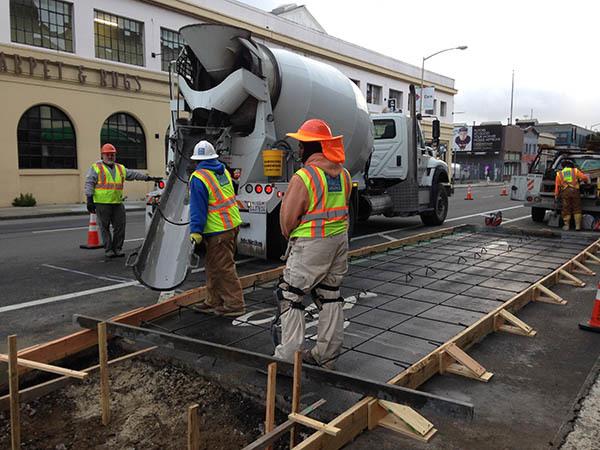 Construction workers pouring concrete for a bus boarding island on a city street.