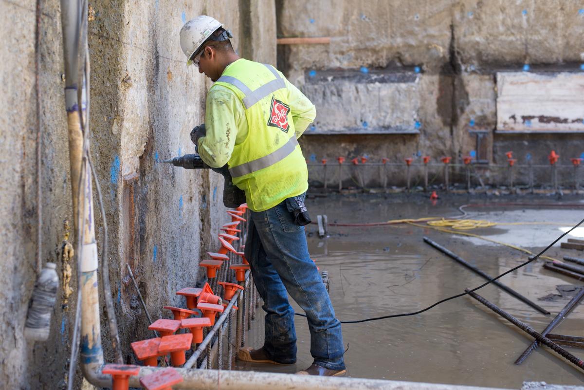 Worker in safety gear drilling into concrete slurry wall to install rebar for headhouse structural construction.