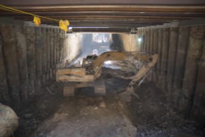 Steel beams and construction materials inside underground station box during roof deck installation.