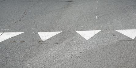 White triangular markings painted on asphalt road surface in a row.