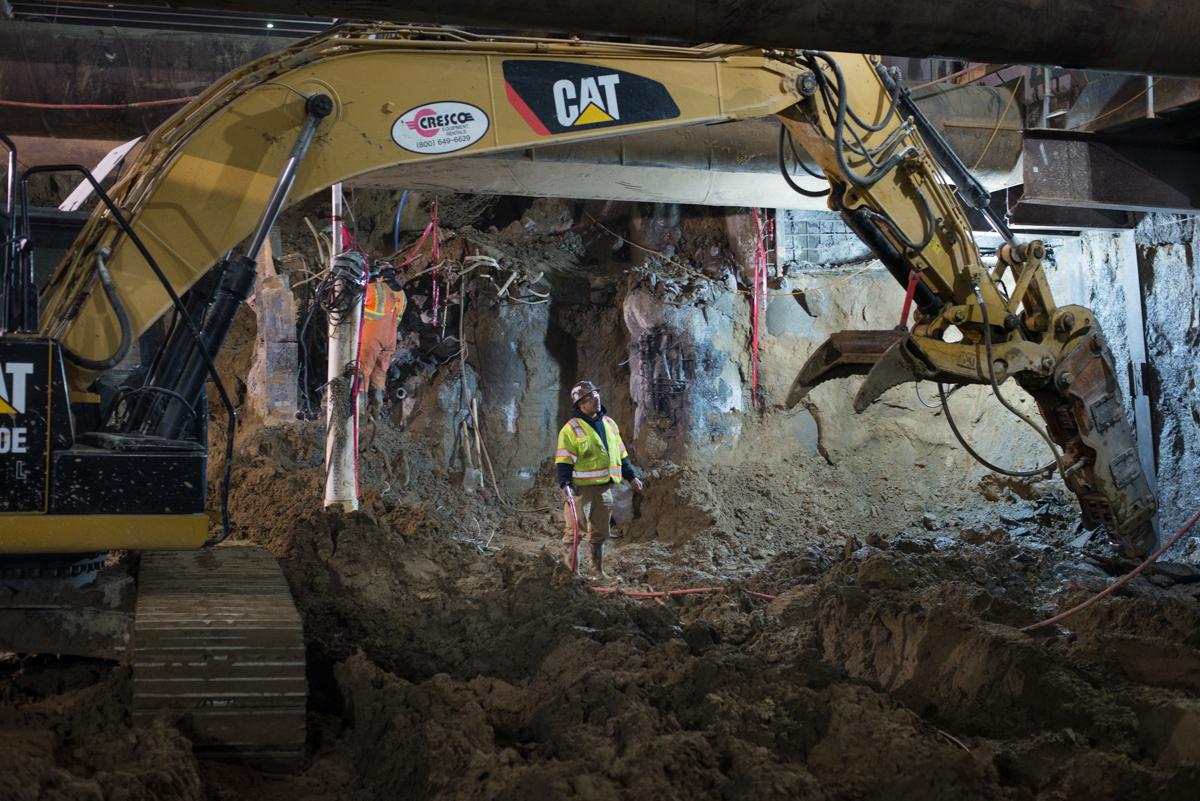 CAT excavator operates in underground tunnel with worker in safety vest during construction work.