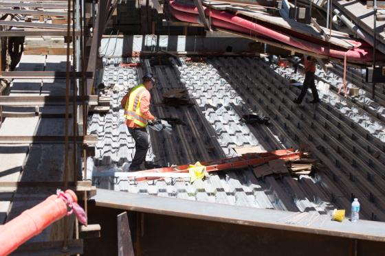 Worker in safety vest inspecting corrugated steel roof deck construction at Union Square Station site.