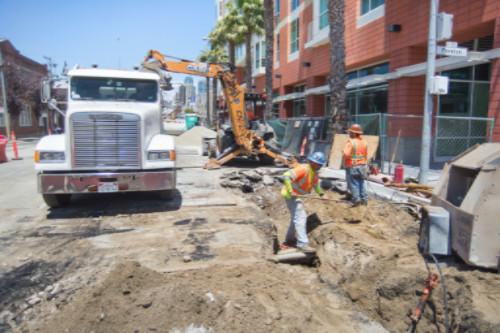Construction crew and equipment excavating street near brick building for tunnel work.